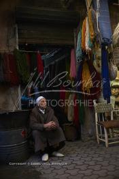 Image du Maroc Professionnelle de  Mohammed Ennaji âgé de soixante-dix ans, pose devant son atelier à Marrakech, il a commencé à pratiquer ce métier de teinturier à l’âge de dix ans, cela lui fait soixante ans de métier un des plus ancien voir le vétéran des teinturiers, son atelier est situé au centre du Souk des Teinturiers, appelé souk Sebbaghine, l'un des plus pittoresque de Marrakech situé dans la Médina, non loin de la source Mouassine, où quelques petits ateliers pratiquent encore de nos jours la teinture traditionnelle. Ce lieu très prisé des touristes et amateurs photos qui désire ardemment des images extrêmement colorées. Avec le temps il est devenu presque une des attractions touristique qui vaut le détour. Derrière Si Mohammed Ennaji des écheveaux de laines sèchent au soleil suspendu en l’air ou le long des murs, le 8 Décembre 2018. (Photo / Abdeljalil Bounhar)